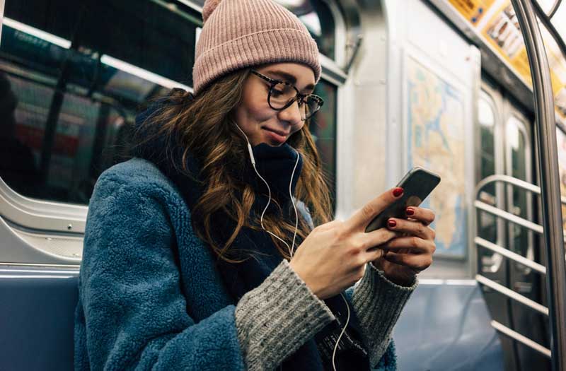 Woman sitting on public transport with earphones looking at a phone